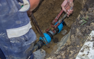 utility workers holds wrench and in trench repair the broken pip