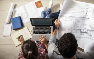 Young couple sitting on the floor and looking at the blueprint of new home.