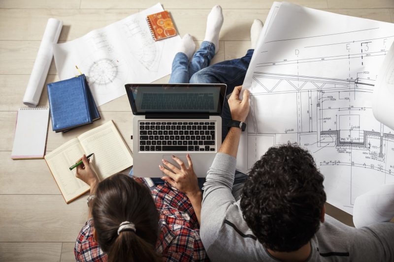 Young couple sitting on the floor and looking at the blueprint of new home.